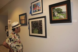 A viewer enjoys works created by paralyzed veterans and civilians. Pictured artwork center  top, “Meeting” mixed media by veteran Don Hyslop, center bottom, “WaterDrops” photography by Claudia Verano Guzzy-DaMetz. Photo by Promise Yee